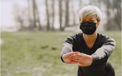 Strong female athlete in medical mask warming up before training in forest during pandemic