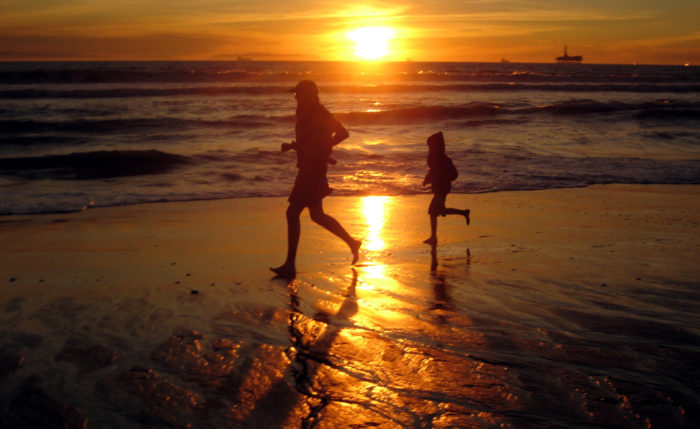 Parent and Child running on beach as sun sets in background